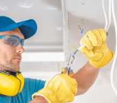Electrician in safety gear using pliers to work on ceiling wiring