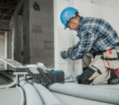 Electrician installing wires in a construction site wearing blue hard hat and plaid shirt kneeling with tools nearby
