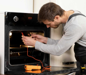Technician testing oven temperature with multimeter, wearing work apron, tool box nearby in bright kitchen setting