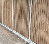 Wooden fence lining a narrow pathway with metal posts visible along the fence structure for outdoor boundary demarcation
