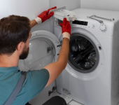 Technician repairing washing machine wearing red gloves in laundry room