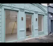 Mint green vintage shopfront exterior with glass windows and door, surrounded by a narrow street in urban setting