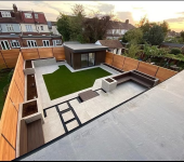 Modern garden design with patio, lawn, seating area, and wooden fence, surrounded by residential houses at sunset