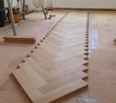 Herringbone parquet flooring installation process in progress at a construction site with tools and planks visible
