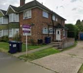 Brick semi-detached house with driveway and front garden in residential UK neighbourhood, estate agent sign visible