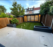 Modern landscaped garden with patio, grass lawn, trees, and a stylish wooden garden room in a residential backyard