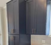 Dark blue kitchen cabinets with gold handles next to a window, featuring white tiled backsplash and bright lighting