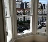 View of a street with terraced houses from a bay window indoors, showcasing classic British architecture and parked cars