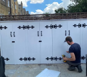 Man installing black hinges on white outdoor wooden storage cabinets