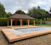 Wooden gazebo and modern swimming pool with timber decking in a lush garden setting