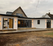 Modern single-storey house extension with large glass doors and a spacious patio area under a cloudy sky