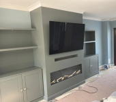 Modern living room with wall-mounted TV, grey cabinets, built-in shelves, and an elegant fireplace design
