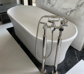 Freestanding white bathtub with chrome tap fixtures set on elegant black marble floor in modern bathroom design