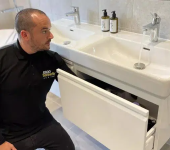 Plumber inspecting under-sink storage in modern bathroom with white fixtures and running tap