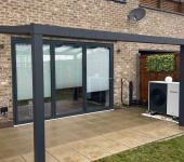 Modern house extension with glass doors and air source heat pump installation in a stylish brick exterior garden setting