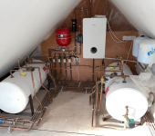 Home boiler system setup in attic with water tanks, red expansion vessel, and pipes, UK residential heating installation