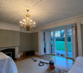 Elegant living room with chandelier, fireplace, and garden view through large windows, decorated in soft neutral tones