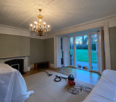 Living room with chandelier, open French doors, fireplace, and vacuum on carpet, overlooking a garden lawn