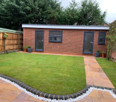 Garden with modern brick shed, patio path, and lawn surrounded by fencing and trees for privacy and aesthetics