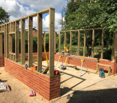 Wooden frame and brick structure under construction amidst trees and blue sky