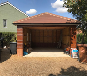 Empty wooden garage with open doors in residential area with parked van, bins, and garden supplies nearby