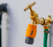 Close-up of a brass outdoor tap with yellow hose connector mounted on wall