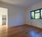Empty room with wooden floor, white walls, open door leading to bathroom, large window with a view of trees