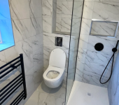 Modern bathroom with marble tiles featuring a wall-mounted toilet, walk-in shower, and black heated towel rail