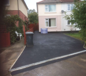 Newly paved driveway leading to a semi-detached house with a visible bin and greenery on the side
