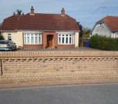 Red-roofed bungalow with brick wall, front driveway, and parked car in a suburban setting