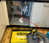 Under-sink plumbing repair with tools and a property repair services sign on a kitchen floor