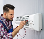 Technician repairing an air conditioning unit on a wall, wearing a plaid shirt and using tools