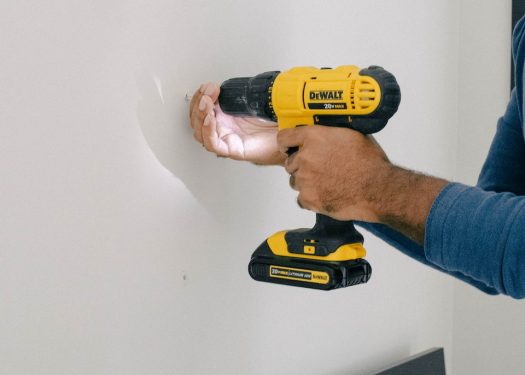 Man using a DeWalt cordless drill on a white wall for home improvement project